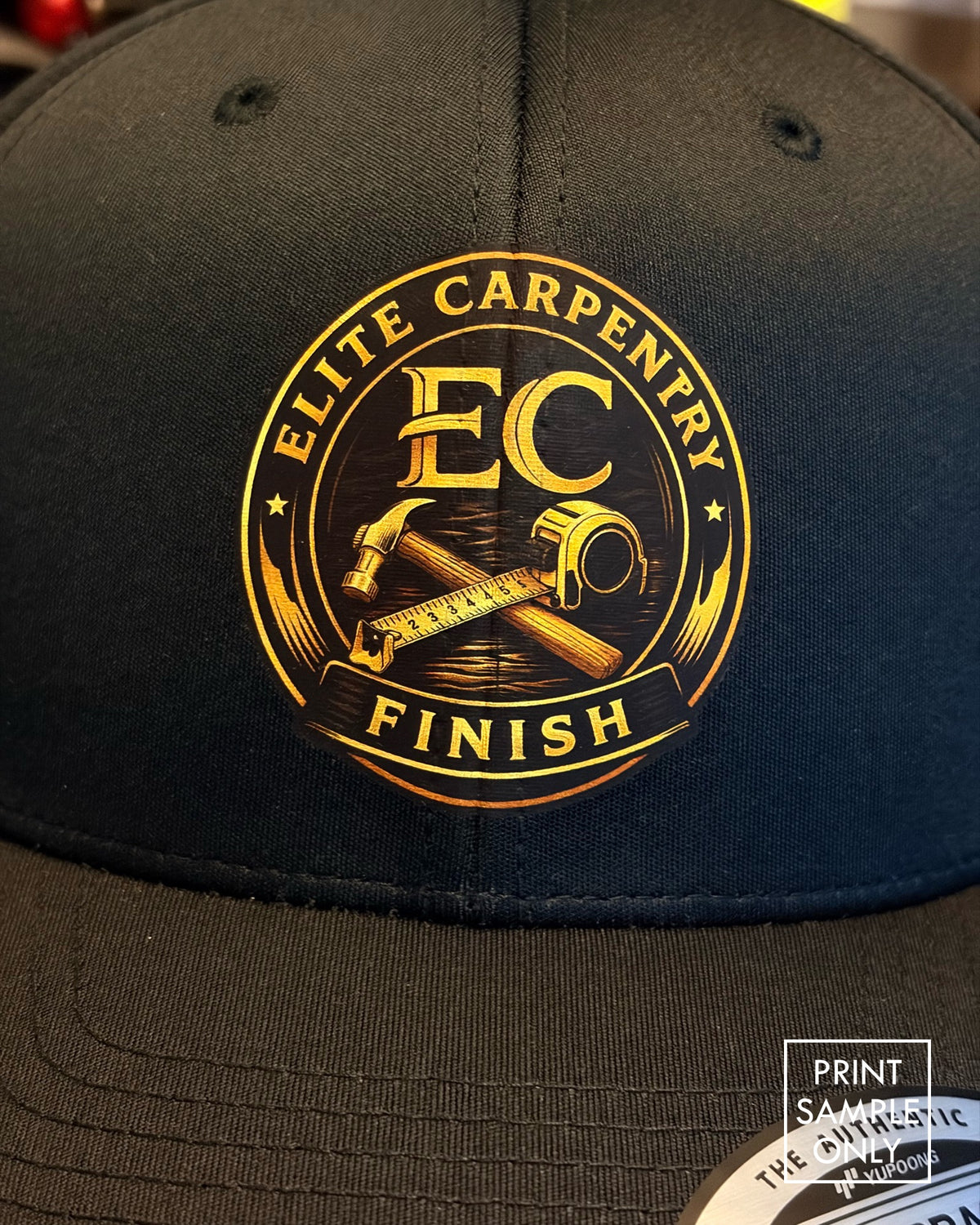 Close-up of a sample print on a black snapback cap: gold crest logo (print sample only)