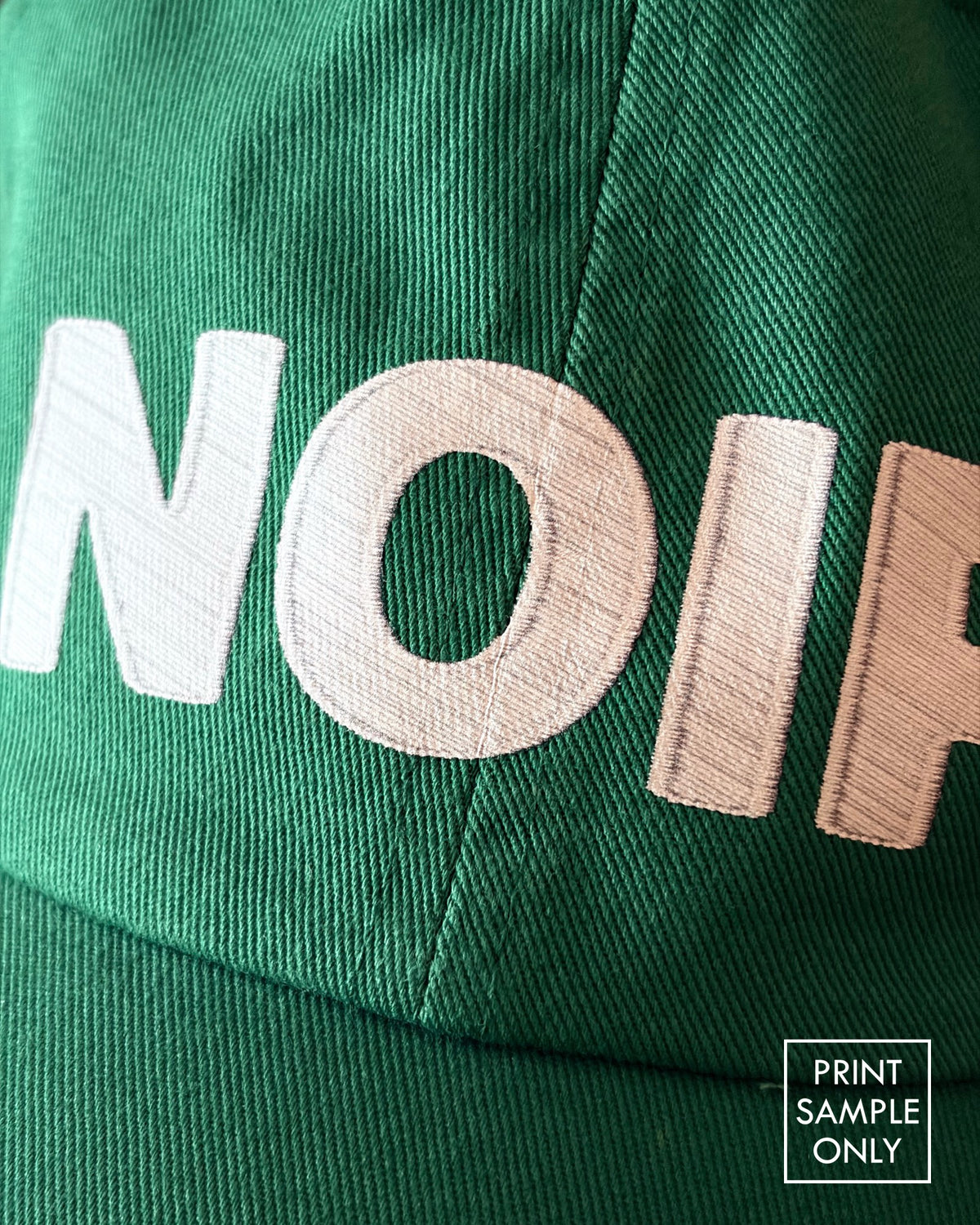 Close-up of a sample print on a green baseball cap: white NOIR lettering (print sample only)