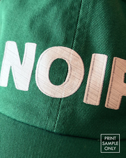 Close-up of a sample print on a green baseball cap: white NOIR lettering (print sample only)