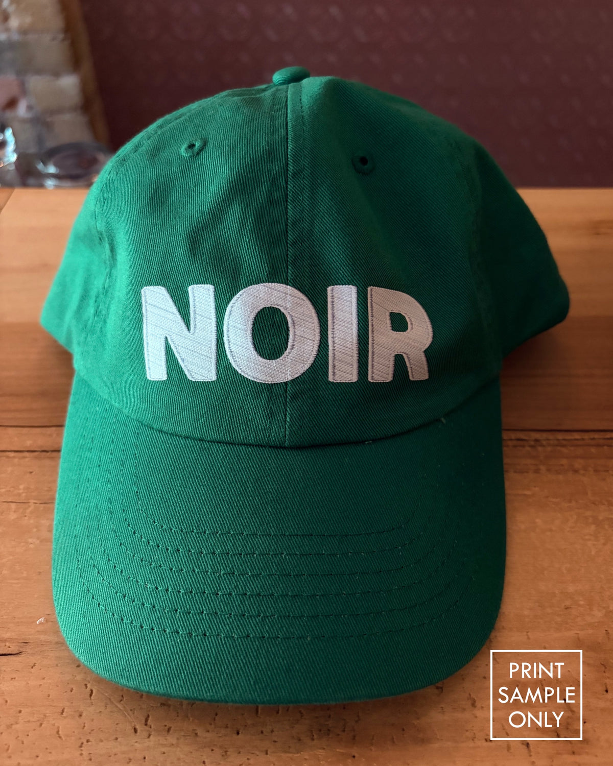 Sample print on a green baseball cap: white NOIR lettering (print sample only)